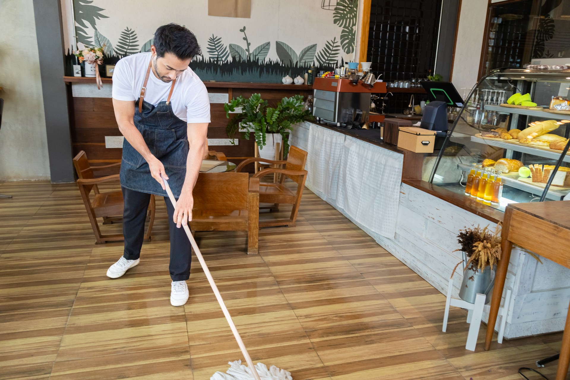 Waiters handsome Indian wearing apron mopping the floor in cafe and bakery preparing to support customers come in restaurant. Cleaning store before closing coffee shop. Small business owner concept.